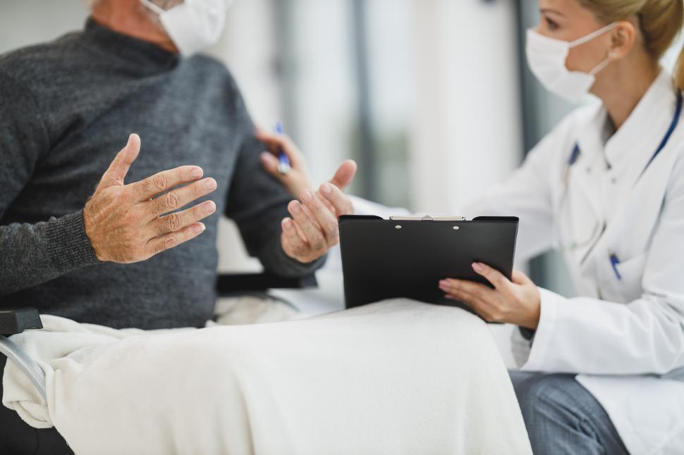 female-caregiver-with-face-mask-talking-to-old-aged-person-in-w